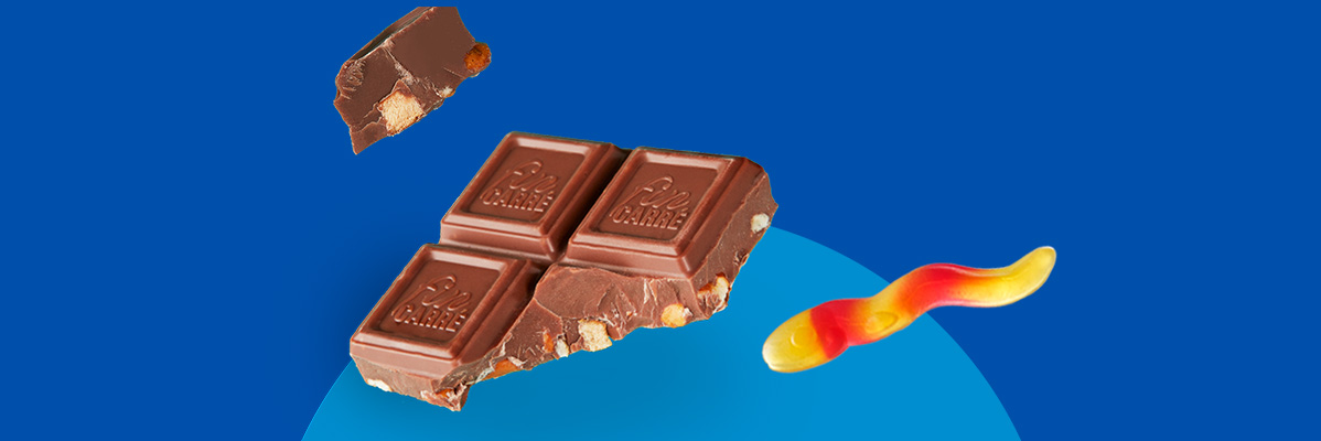 Chocolate bar pieces with nuts and a red and yellow gummy candy on a blue background.