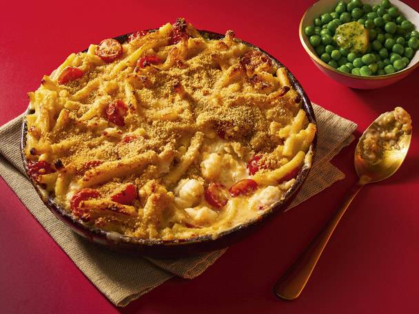 Baked macaroni and cheese with tomatoes, served with a side of peas and a spoon.