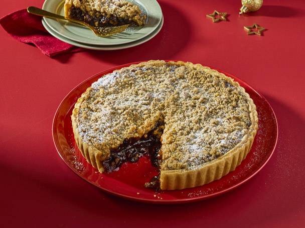 Mince pie tart with a slice on a plate, festive decorations on a red background.