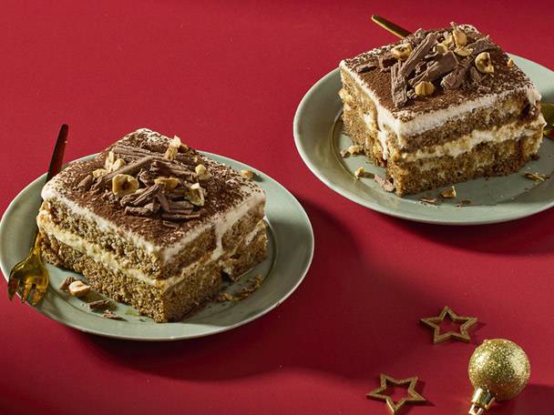 Two slices of tiramisu cake with chocolate shavings and hazelnuts on green plates.