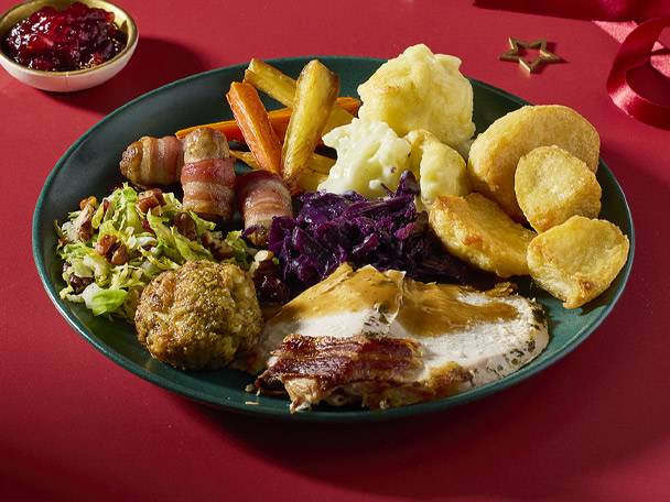 A festive Christmas dinner plate with turkey, roast potatoes, pigs in blankets, and vegetables.