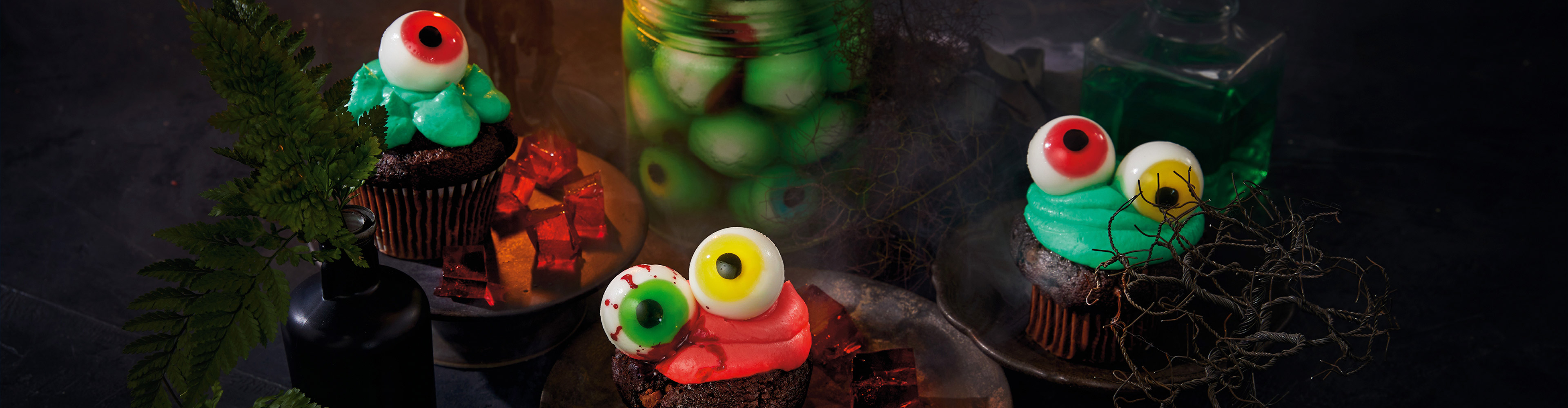 Halloween cupcakes and candies with eyeball decorations, a candle, and a green potion bottle.