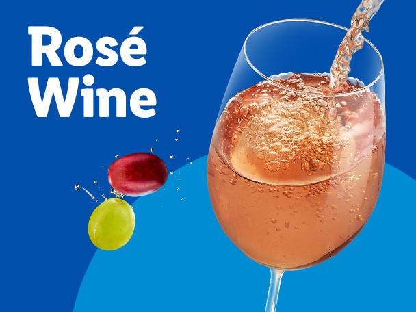 Rosé wine being poured into a glass, with red and green grapes nearby.