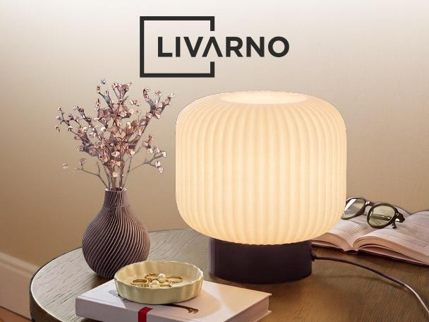 A glowing ribbed table lamp on a wooden side table next to a decorative vase and books.