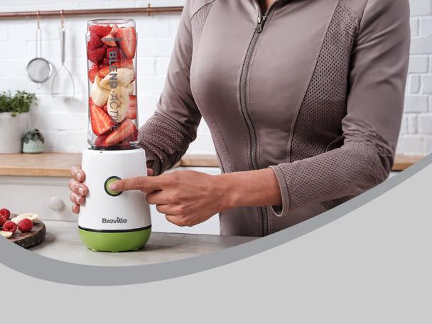 Woman blending strawberries and bananas in a personal blender on a kitchen counter.