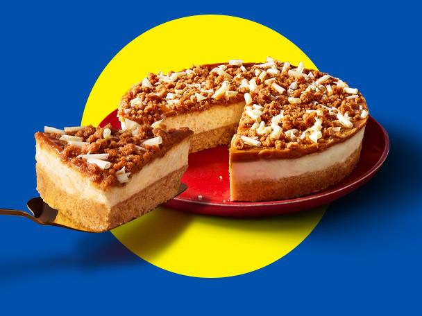 Cheesecake with a slice being served, topped with caramel and crumble, on a red plate.