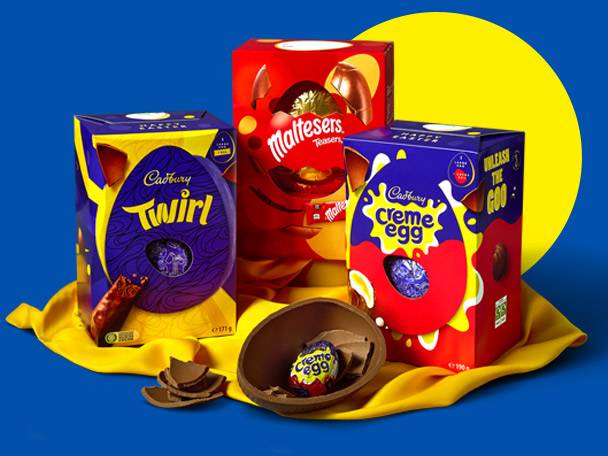 Three chocolate Easter egg boxes, including a purple one and a red one, on a yellow cloth.