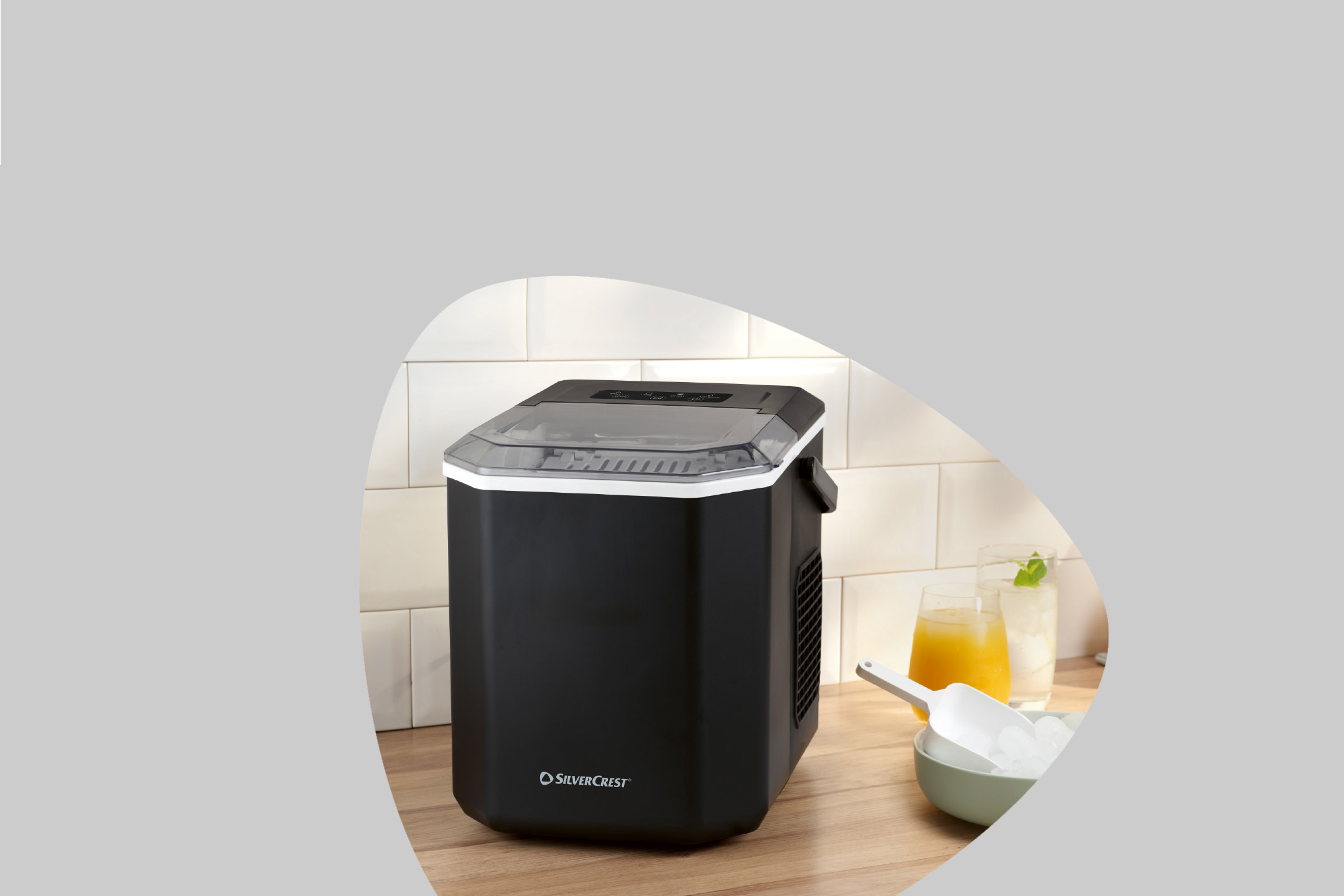 Black ice maker on a wooden counter with drinks and a bowl of ice.